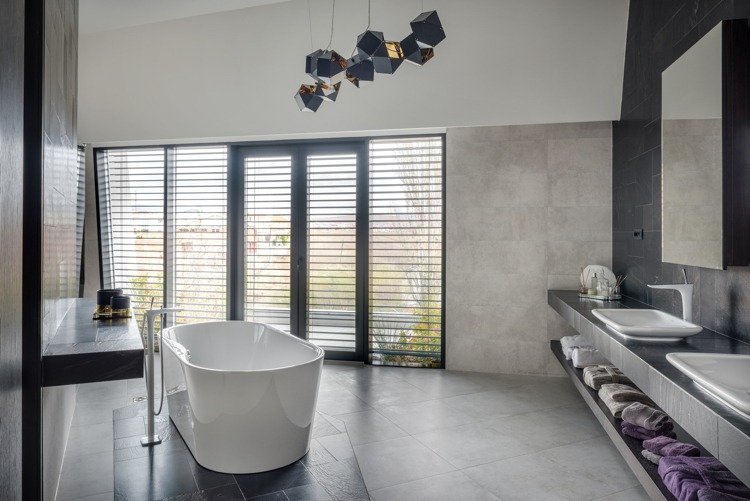 Badrum med oregelbunden planlösning i grå nyanser, fristående badkar