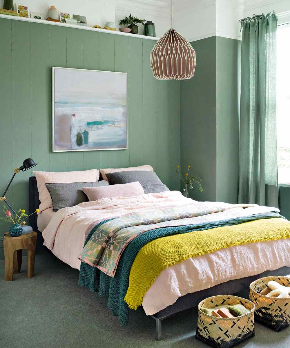 Olivgrön vägg i sovrummet i trä och färgglada sängkläder
