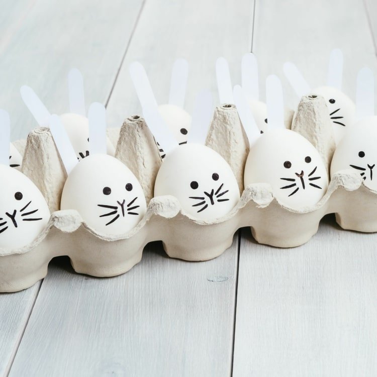 Påskkaniner gör hantverk med småbarn på påsk - målar påskägg och lägger kaninöron på dem
