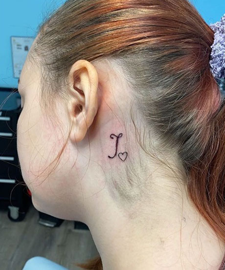 Vaikuttava J -tatuointi korvan takana