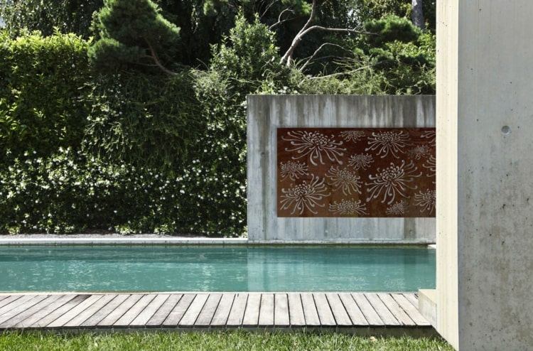 Minimalistisk trädgårdsdesign vid poolen med sekretessskärmar i Cortenstål inramade i exponerad betong