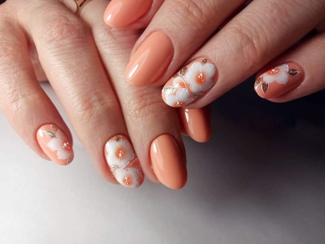 Aprikosgel naglar i kombination med vita blommor