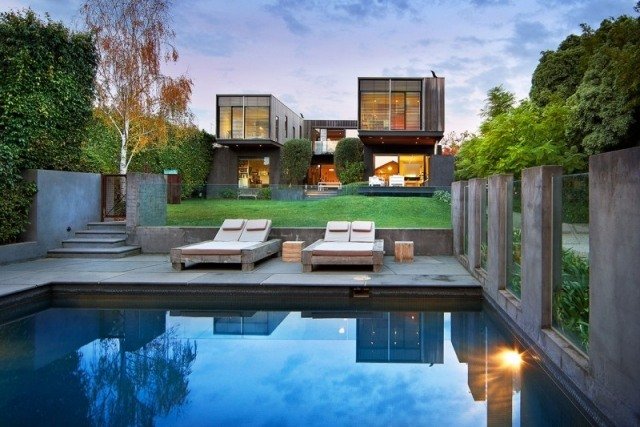 modernt hus pool terrass solstolar betongglas trädgårdsvägg