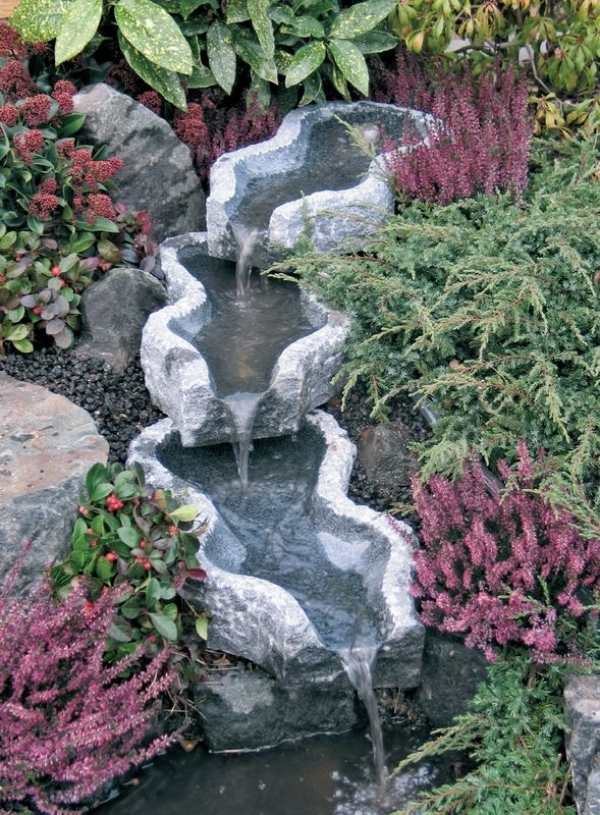 konstnärligt utformade vattenfall stenar vatten trädgård färgglada blommor