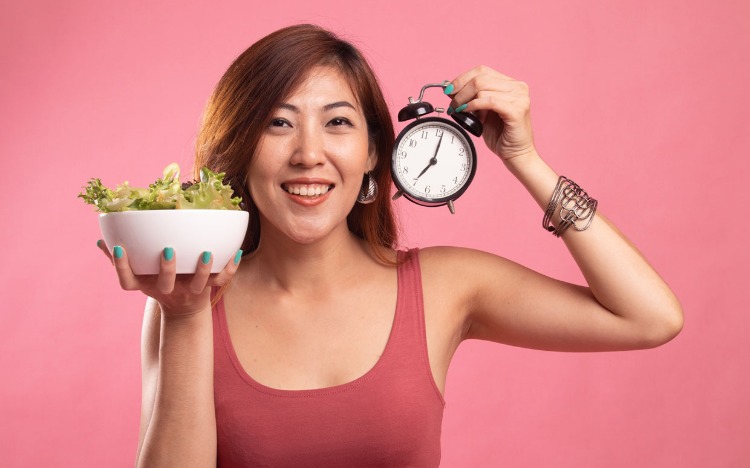 asiatisk kvinna med skål med sallad och väckarklocka i handen intermittent fasta
