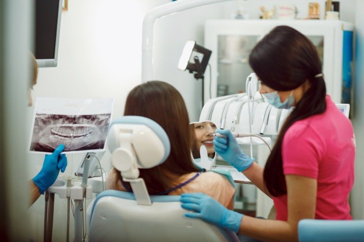 leende ung kvinna tittar i spegeln medan hon sitter på tandläkarstolen under behandlingen