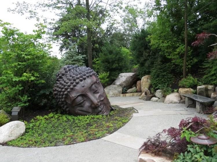 asiatisk-trädgård-dekoration-buddha-staty-metall-bänk-sten-gröna-träd-trädgård-stenblock