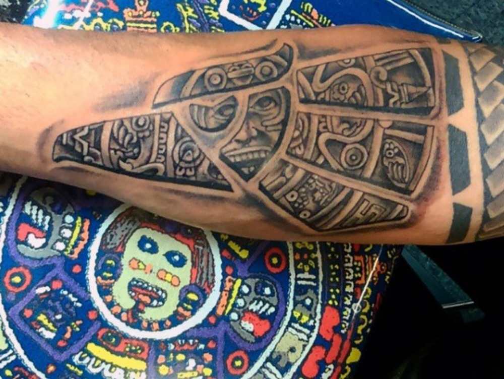 Insidan av underarmen tatuerad med aztec -symboler på färgad bas