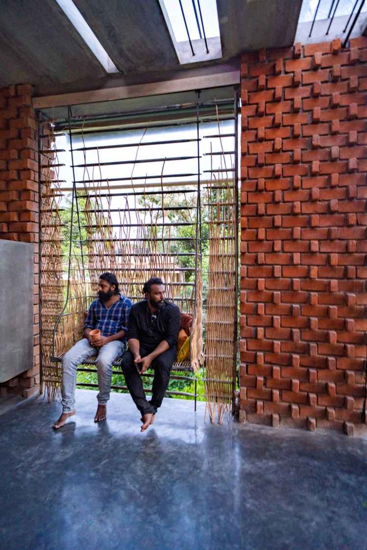 två arkitekter från wallmakers arkitektkontor sitter på en gunga i det nybyggda huset med en tegelvägg inuti