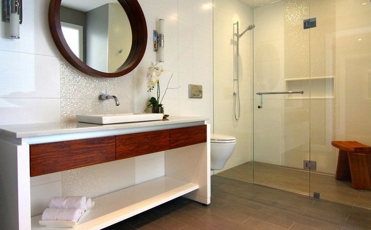 Rund spegel i badrummet med duschkabin och glasdörr framför duschnisch av kaklat handfat