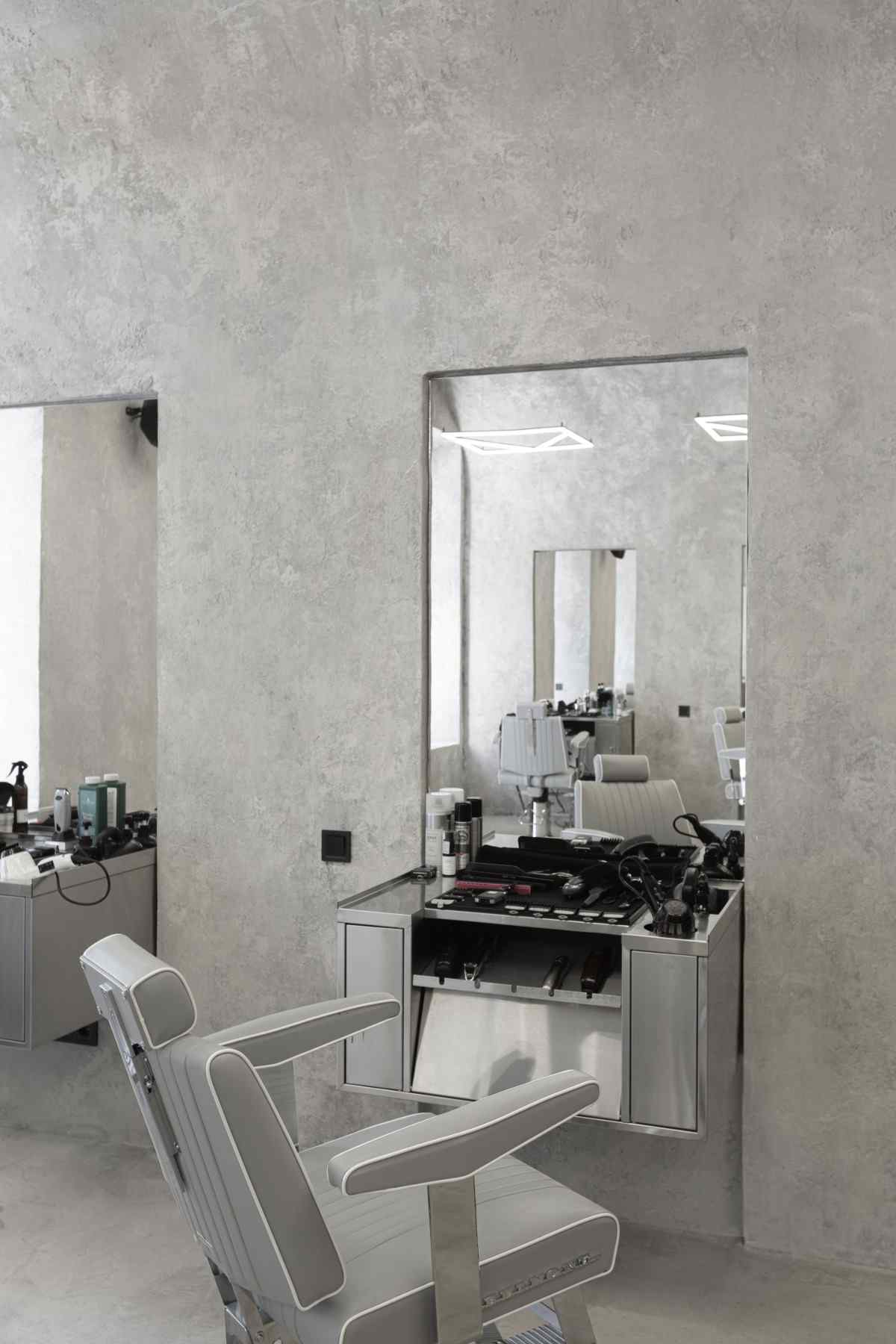 stor spegel i frisörsalongen med snurrstol i grått läder och dekorativt väggpanel i gips