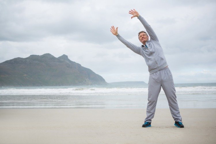 Gråhårig man på stranden gör stretching magen bort träning män över 50