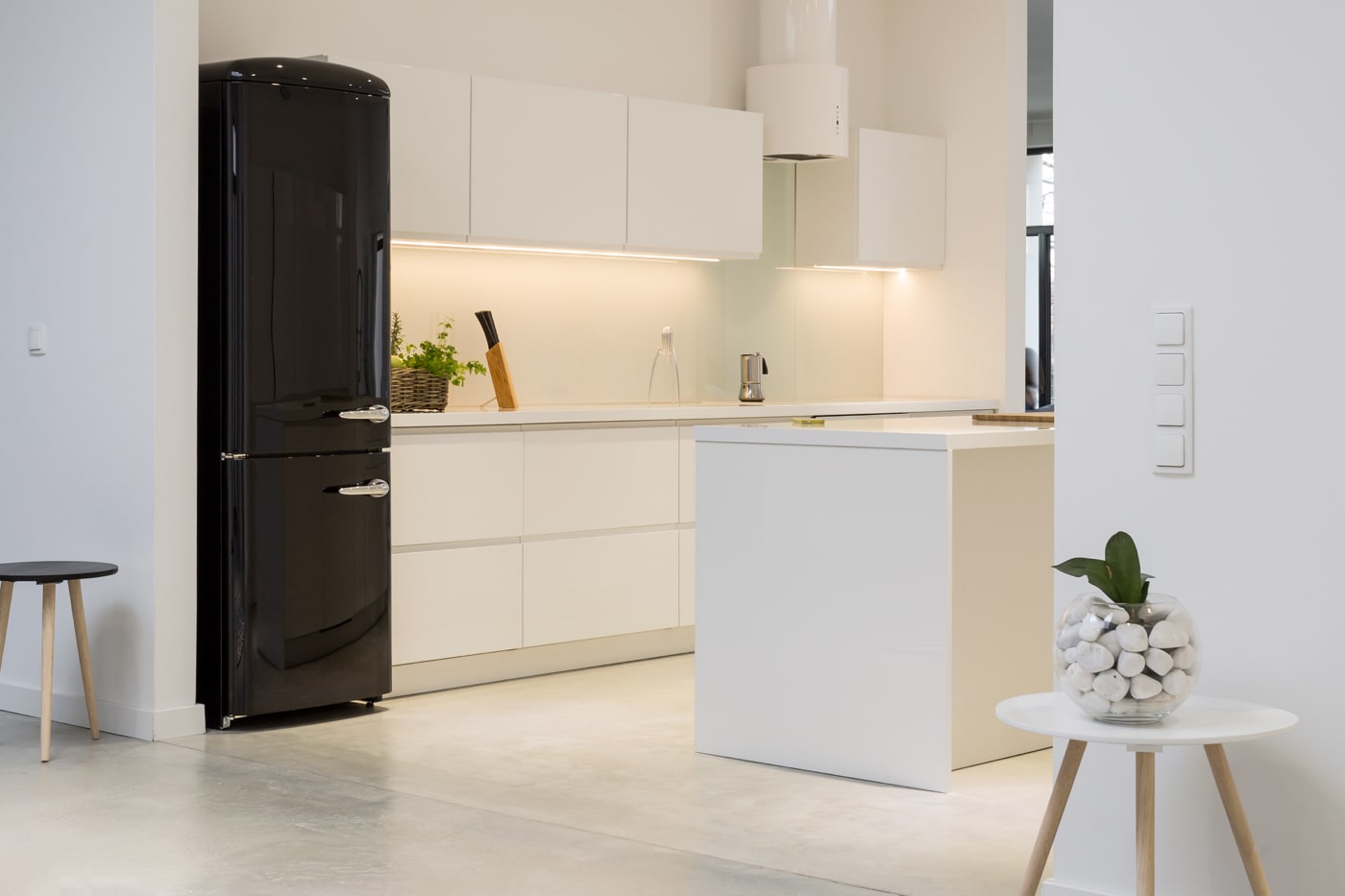 minimalistiskt vitt kök med ö och svart kylskåp