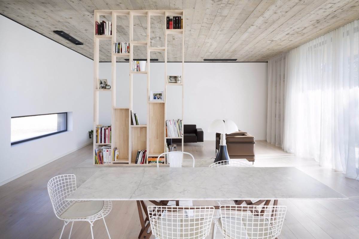 interiör i maison 0 82 med bokhylla av trä, marmorbord, betongtak och stora fönster