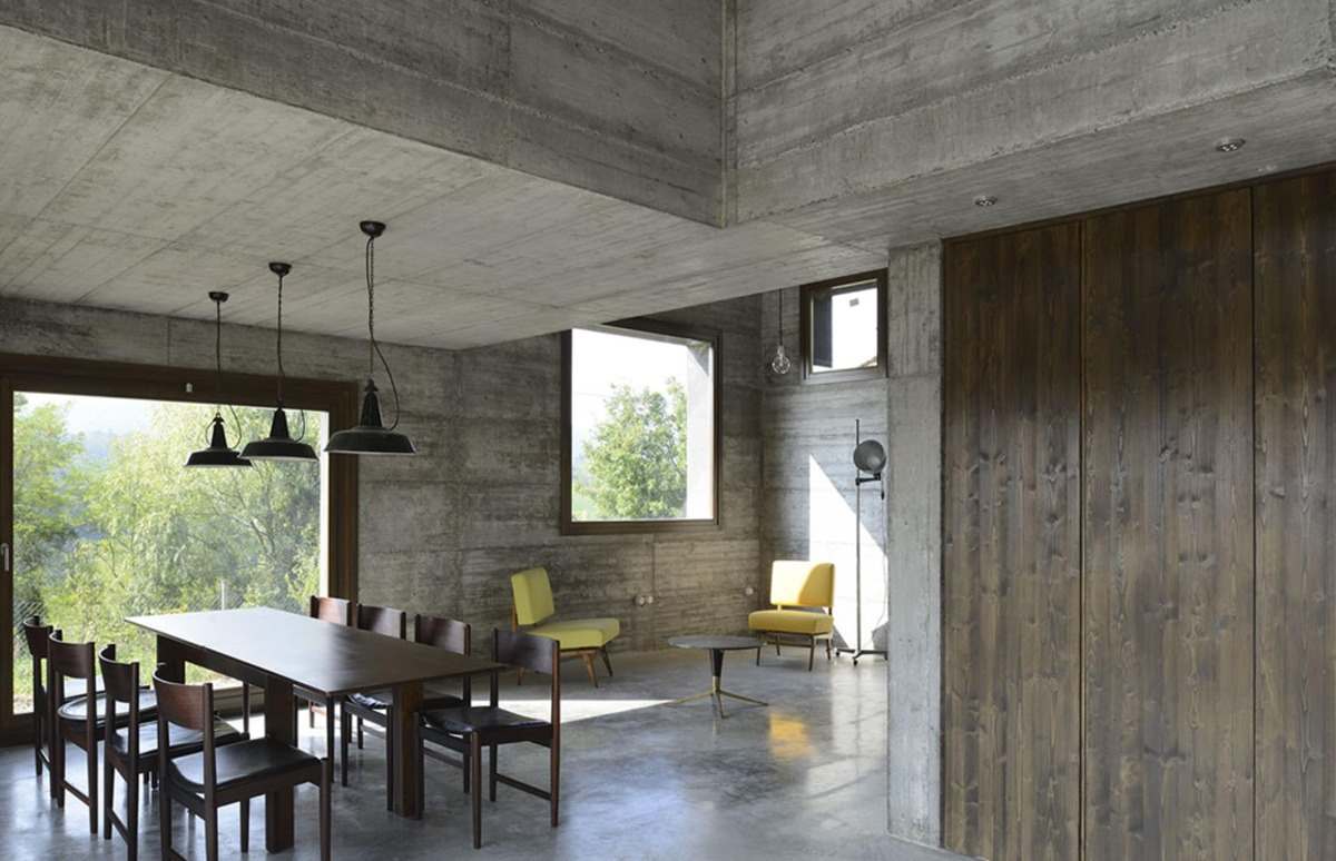 Stort öppet vardagsrum med matbord i trä och gula stolar i betonghuset
