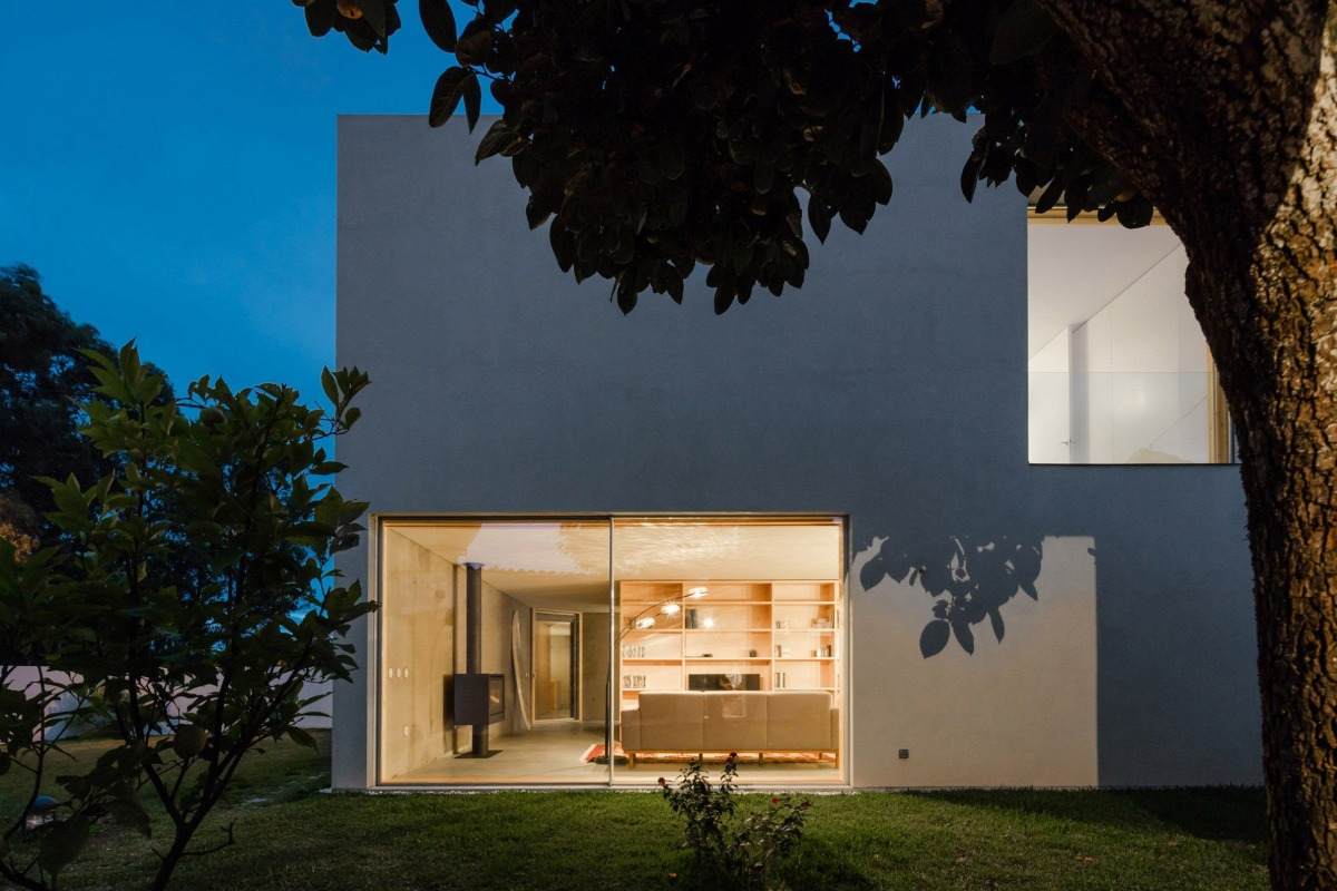 minimalistiskt hus med vit fasad och stora fönsterträd i kvällsljuset