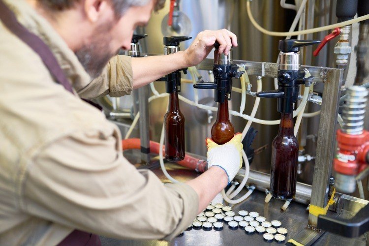 Fyll ölflaskor med en maskin i en fabrik medan du brygger öl själv