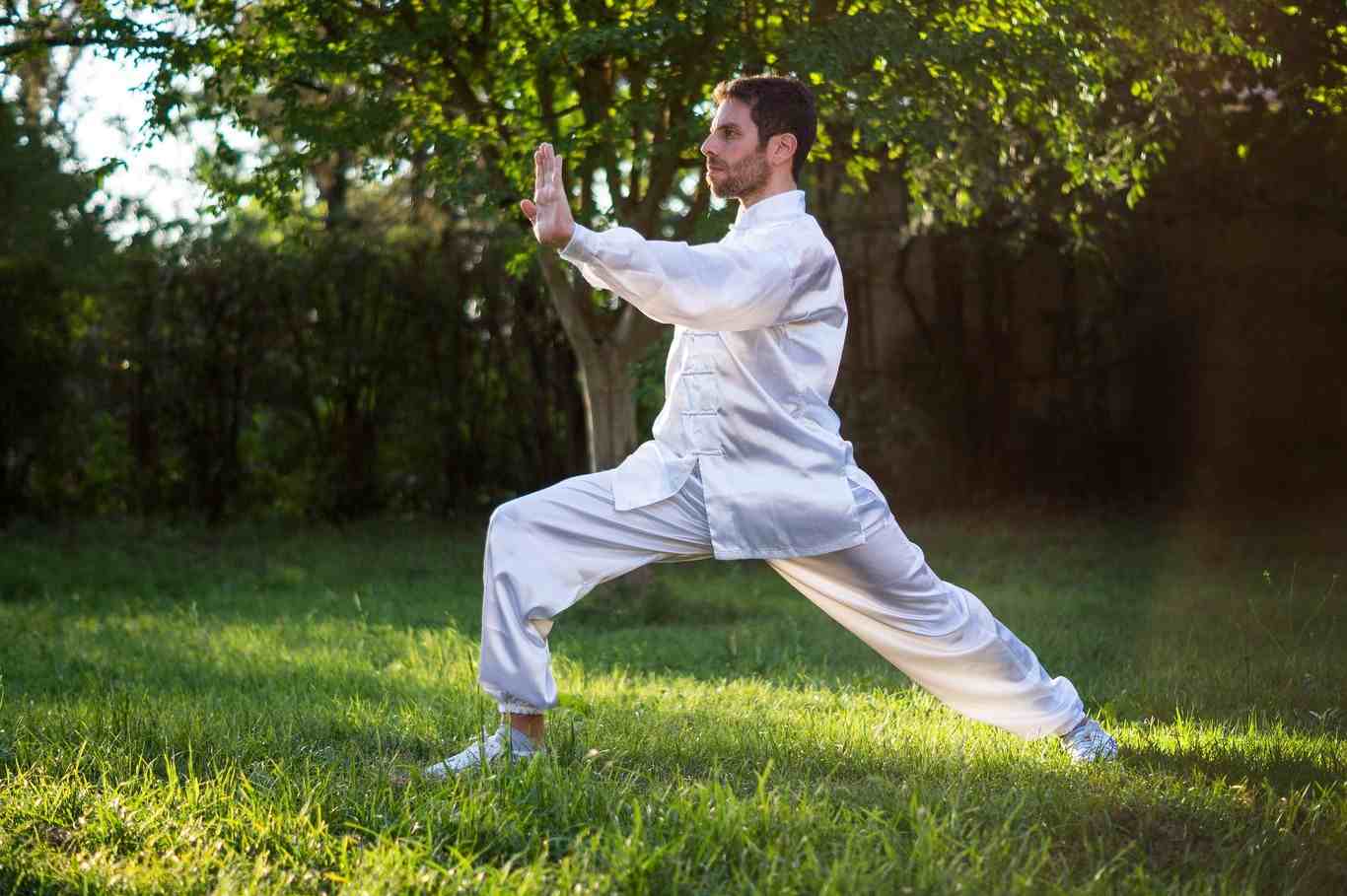 man i vit tai chi -kostym utövar kampsport i skogen