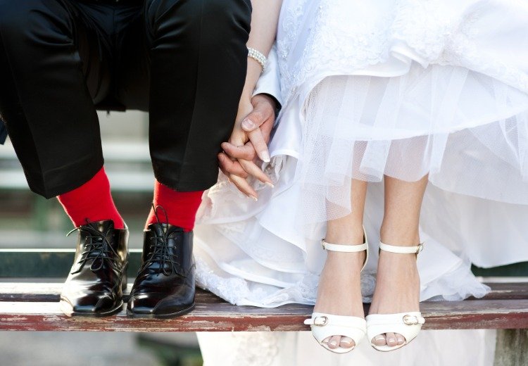 ljusröda strumpor som en accent i bröllopsdräkten för brudgummen med bruden i vit klänning