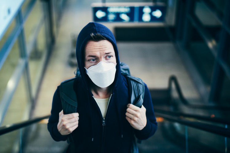 ung man på rulltrappa på flygplatsen bär ansiktsmask som skydd under corona -resa