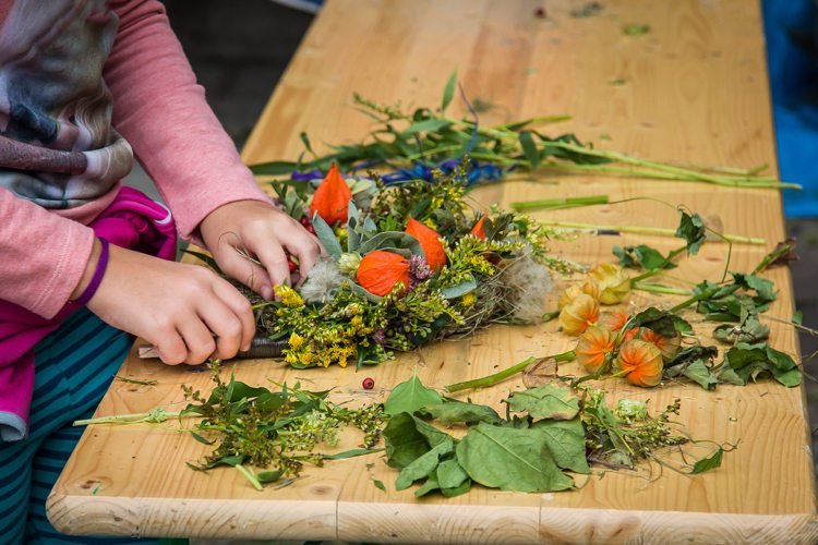 Ett barn knyter en höstkrans av ängsblommor, kvistar och lyktblommor