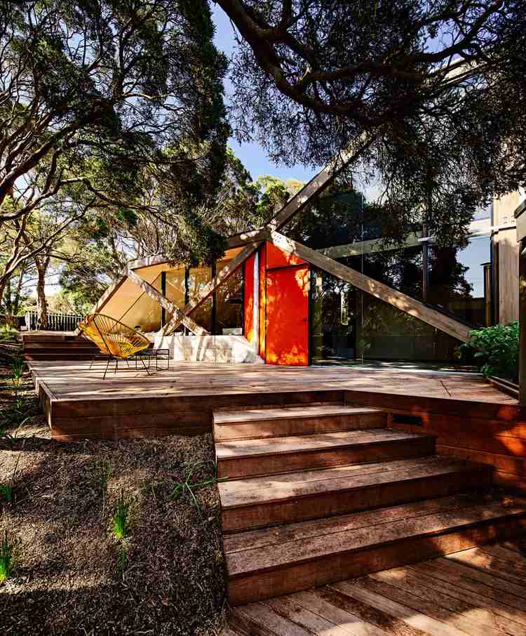design fritidshus sluttande kust kust skog modern fjällstuga ovanlig form trä veranda entrédörr orange