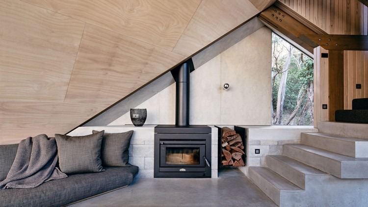 design fritidshus sluttande tak kust skog modern fjällstuga ovanlig form soffa öppen spis betong trappor