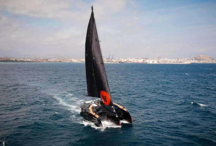 designer tre-skrovs båt med svarta segel i vattnet