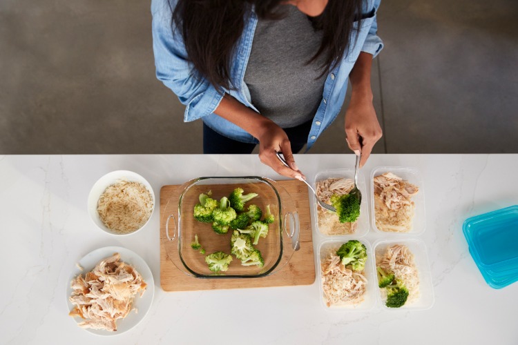 kvinna förbereder portioner mat från broccoli och kyckling för den perfekta kosten