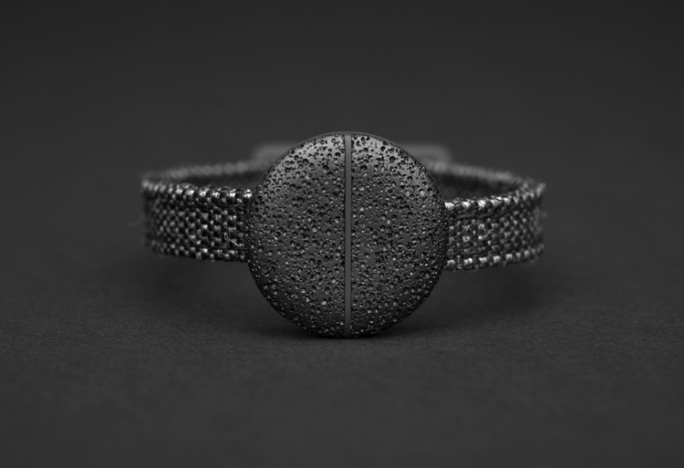 digitalt plånboksmynt av svart-poröst aluminium fäst vid ett armband