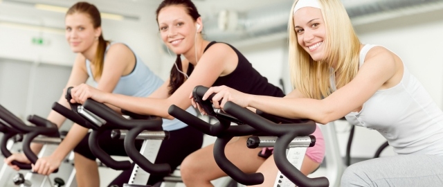 tre-kvinnor-i-fitness-på-fitness-cykel