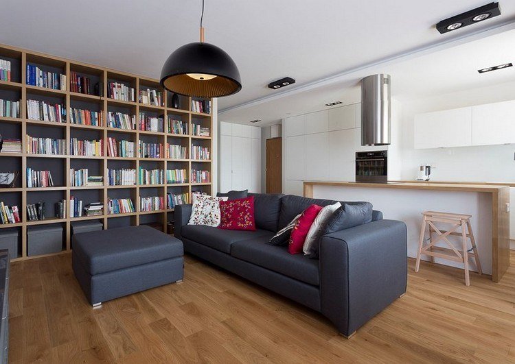 modernt vardagsrum-soffa-antracit-trägolv-röda kuddar-vitt-kök