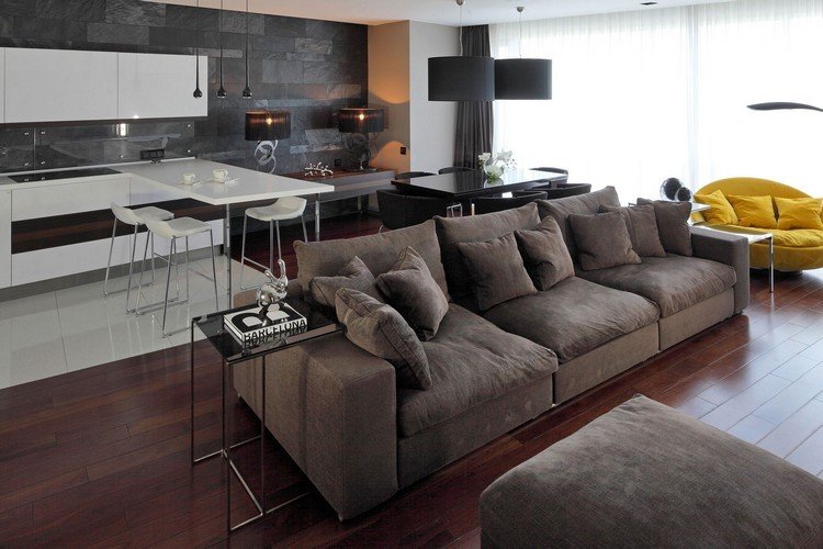 modernt vardagsrum-soffa-brunt trägolv-vitt-kök-gråvägg