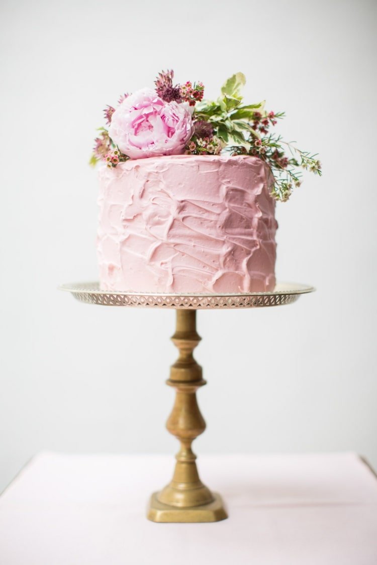 Vacker bröllopstårta i rosa med belagd grädde på en hög stativ