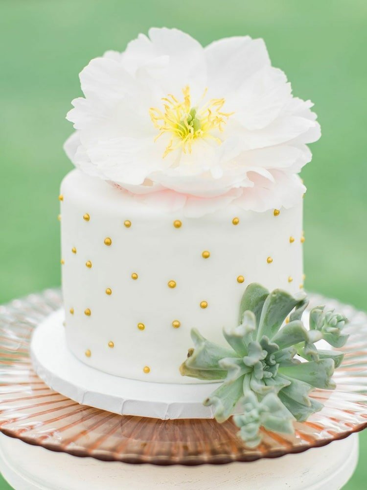 Vit bröllopstårta dekorerad med guldpärlor och stor blomma och saftig växt