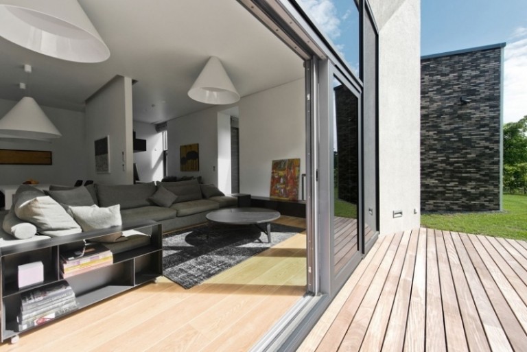 Inredning-vardagsrum-öppen-trädgård-glas-vägg-soffa-grå-lampor-kon-vit