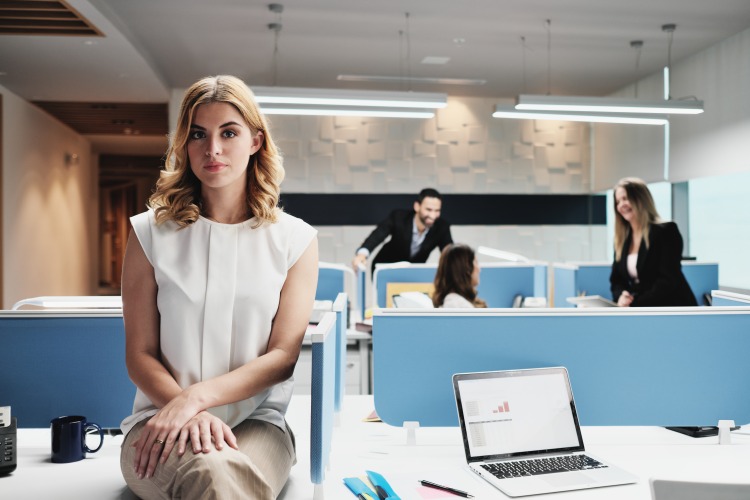 kvinna som sitter ensam vid skrivbordet på kontoret bredvid kollegor