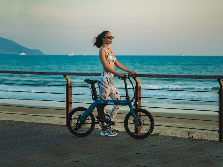 kvinna med vikbar elektrisk cykel njuter av solnedgången på stranden