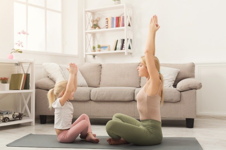mamma och hennes dotter gör yogaövningar tillsammans i vardagsrummet