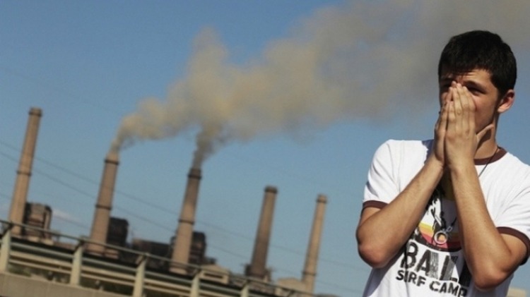 ung man täcker näsan på grund av luftföroreningar från en fabrik