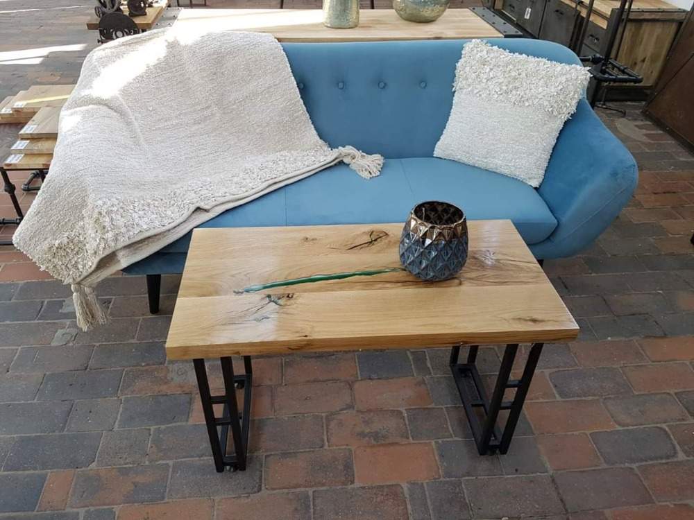ljusblå soffa med filt och kuddar bakom soffbord av trä och epoxi