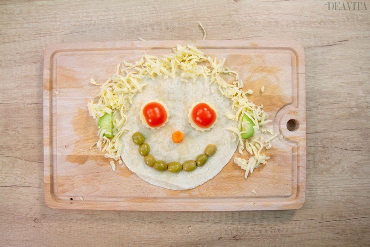 Tortillas ansikte med grönsaker, ost och oliver
