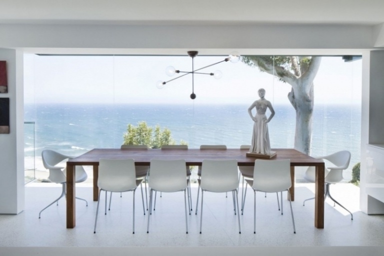 Matsalsmöbler -vit-träbord-plast-stolar-lysande-glas-vägg-utsikt-hav-staty