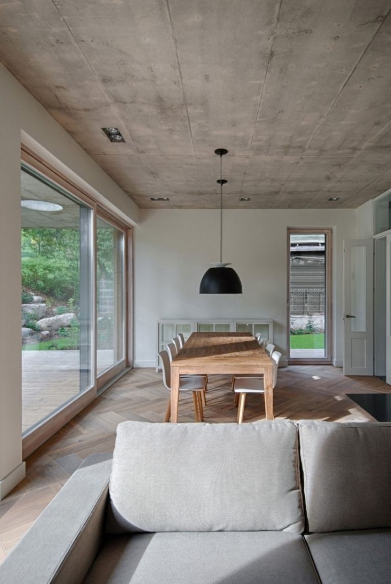 matsal-möbler-soffa-grå-matbord-stolar-vit-hängande-lampa-betong-tak-glas-fönster-