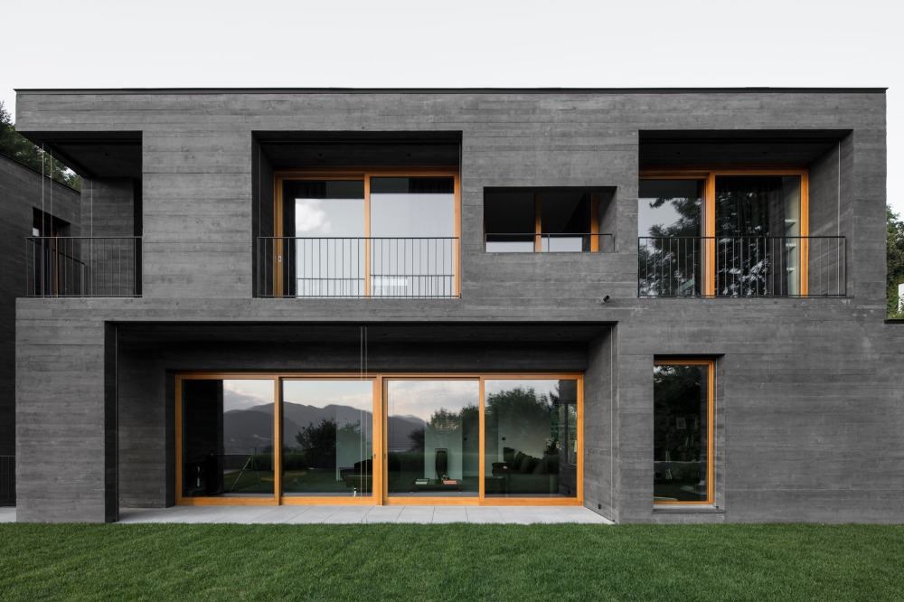 modern villa gjord av svart betong i kontrast med trästommar av fönster