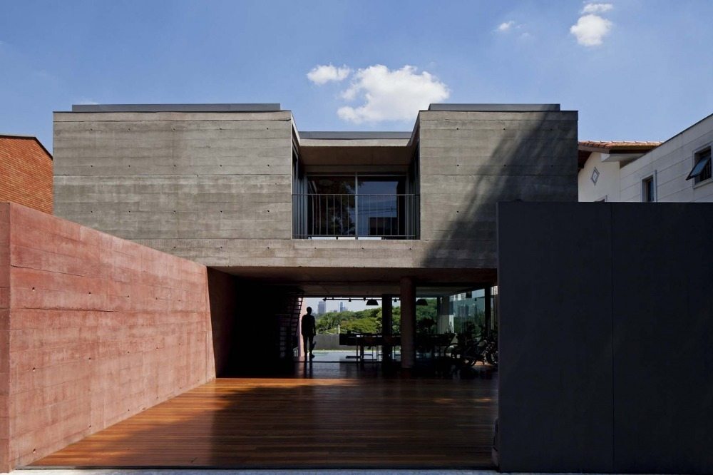 Trägolv på utsidan med en vägg av rödfärgad betong i ett minimalistiskt hus