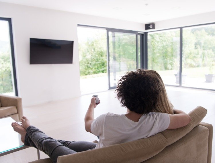 paret sitter i soffan och slår på platt -tv på väggen