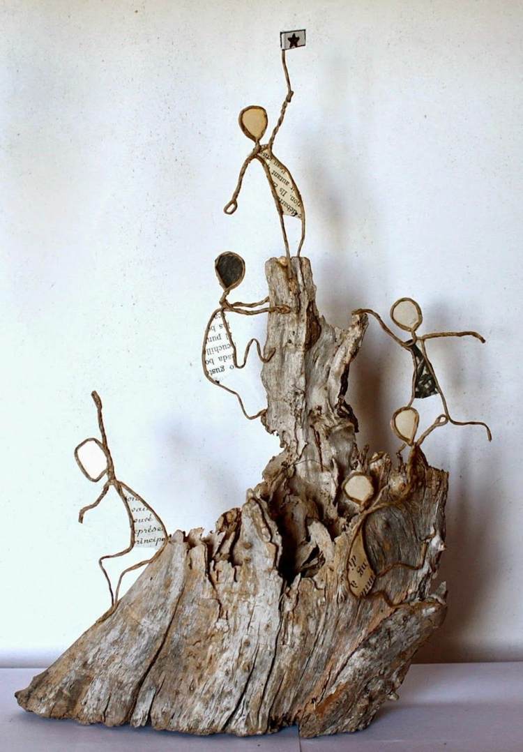 Papperstrådsfigurer klättrar upp på ett berg av trä