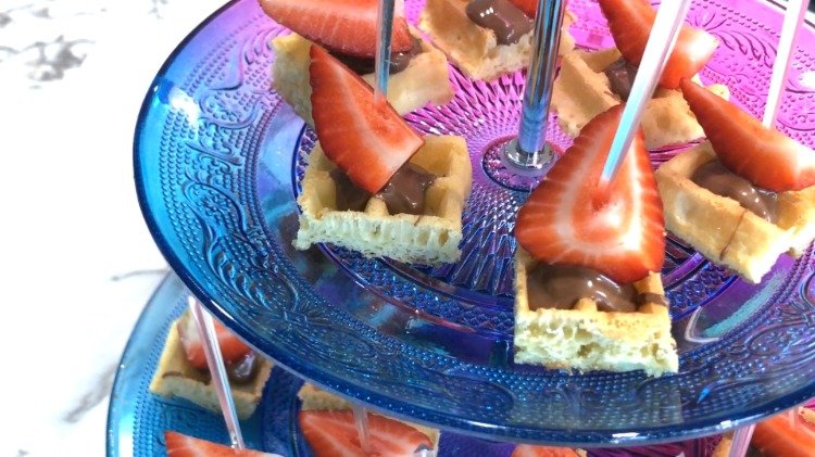 Bettstora fingermatsnacks gjorda på våfflor, jordgubbar och choklad med en festplockare i en tallriksparty