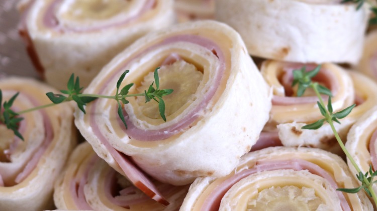 Fingermatsnacks gjorda av rullade tortillainpackningar med skinka och ost, dekorerade med persilja eller krasse